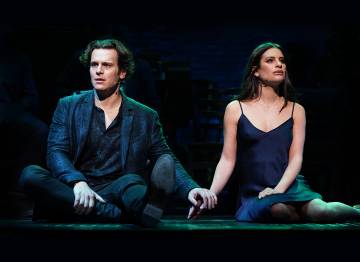 Jonathan Groff and Lea Michelle sitting on stage and holding hands as they perform at the Spring Awakening reunion show.