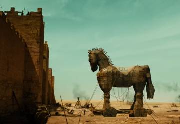 A trojan horse is waiting outside of a city's walls with debris scattered around from a recent battle.