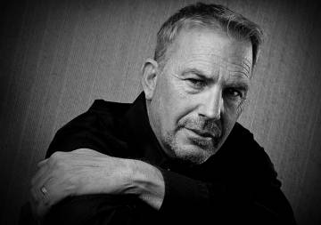 A close up black and white headshot of Kevin Costner crossing his arms.  