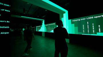 Four people are standing in a dark room with bright green graphics of data reports specific to life in New York City.