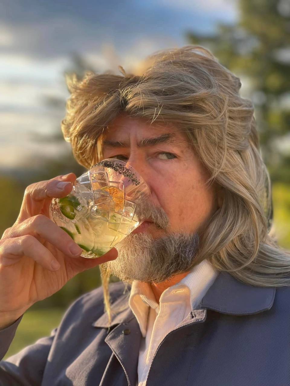 Director Steve Miller, drinking from a pepper-rimmed cocktail glass, golden sunlight illuminating his face as he looks slyly to his left.